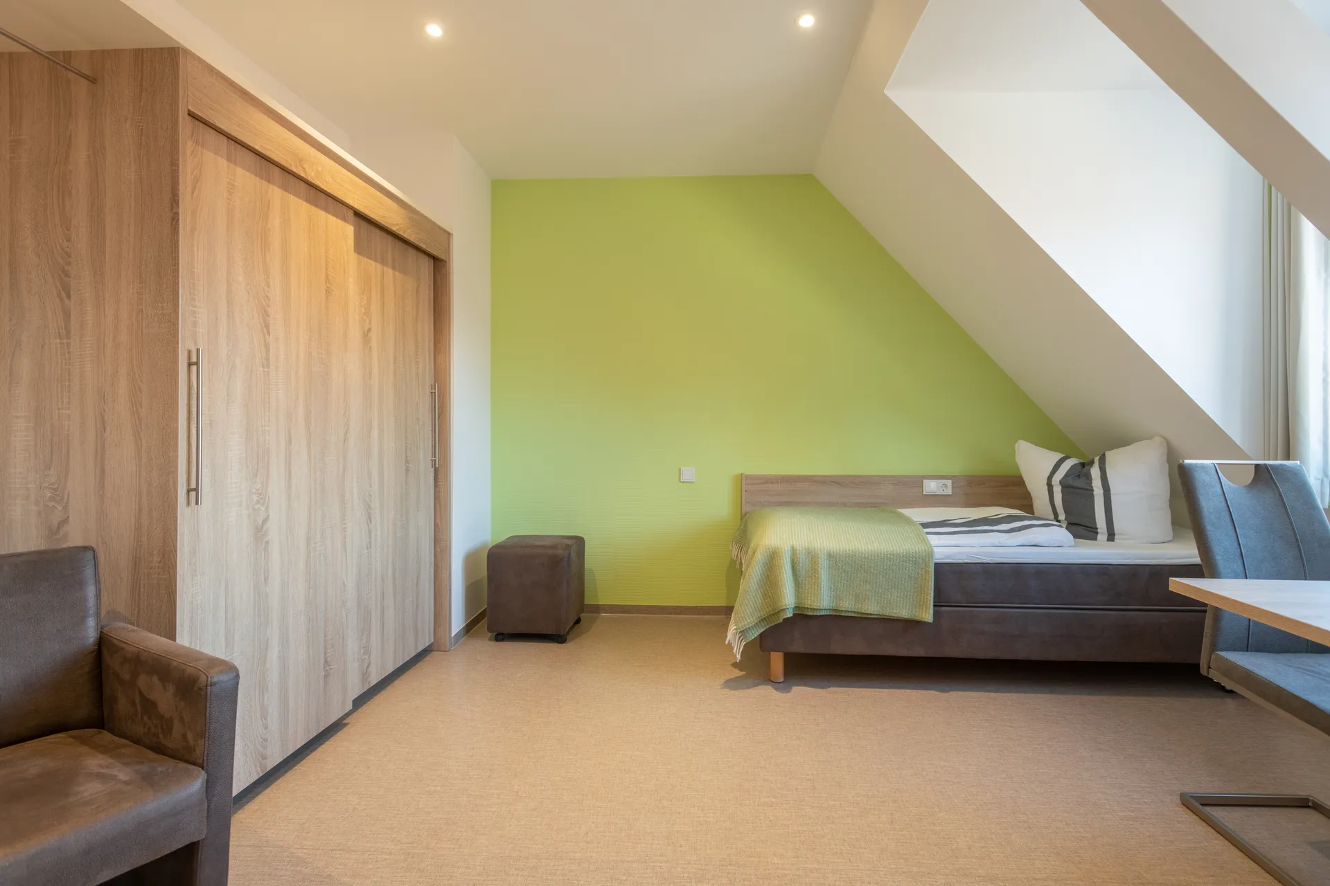 Möbliertes Apartment im Cityapart Heiligenstadt mit Doppelbett, Schrank und Sitzbereich unter dem Dachschrägen-Fenster.