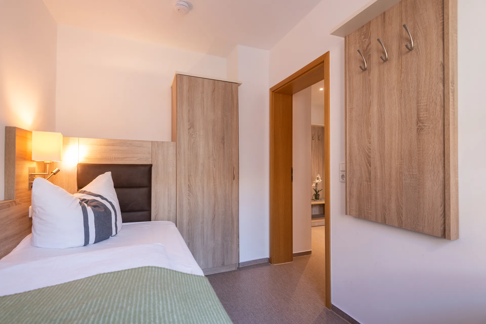 Möbliertes Apartment im Cityapart Heiligenstadt mit Schlafbereich, Kleiderschrank und Blick in den Flur mit Garderobe.